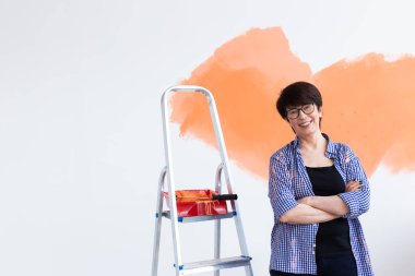 Yeni dairesinde duvar boyayan orta yaşlı güzel bir kadın. Yenileme ve dekorasyon konsepti. Boşluğu kopyala.