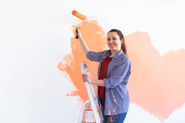 Yeni evin duvarlarını boyayan neşeli bir kadın. Yenileme, onarım ve dekorasyon konsepti. Boşluğu kopyala.