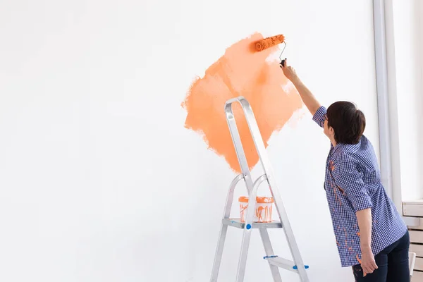 Piuttosto sorridente donna di mezza età pittura parete interna della casa con rullo di vernice. Ristrutturazione, ristrutturazione, riparazione di appartamenti e concetto di ristoro. Copia spazio. — Foto Stock