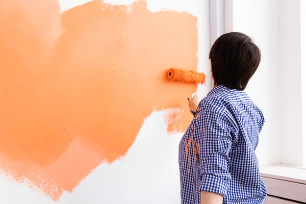 Orta yaşlı güzel bir kadın boya rulosuyla duvarı boyuyor. Yeni dairesinde duvar boyayan güzel bir kadının portresi. Dekorasyon ve yenileme konsepti. Arka plan.