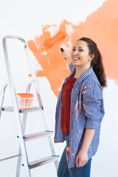 Reparación en el apartamento. Mujer feliz pinta la pared con pintura. — Foto de Stock