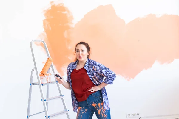 Bailando divertida mujer pintando la pared con rodillo de pintura. Retrato de una joven mujer hermosa pintando la pared en su nuevo apartamento. Concepto de reacondicionamiento y renovación. — Foto de Stock