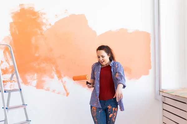 Reparatie in het appartement. Vrolijke vrouw schildert de muur met verf. — Stockfoto