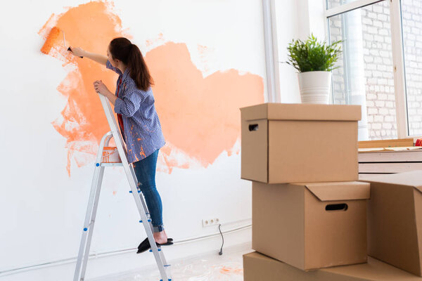 Pretty smiling woman painting interior wall of home with paint roller. Redecoration, renovation, apartment repair and refreshment concept.