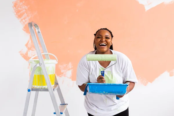 Sorridente donna afroamericana pittura parete interna della casa. Concetto di ristrutturazione, riparazione e ridecorazione. — Foto Stock