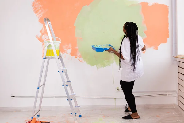 Reparaţii în apartament. O tânără fericită pictează peretele cu vopsea . — Fotografie, imagine de stoc