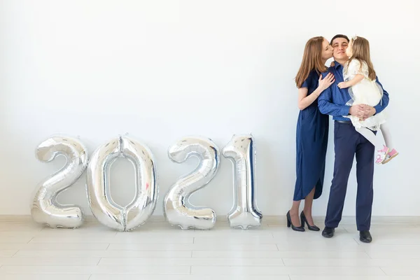 Joven familia feliz madre y padre e hija de pie cerca de globos en forma de números 2021 sobre fondo blanco. Año nuevo, Navidad, vacaciones — Foto de Stock