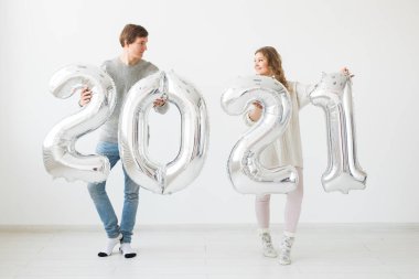 Tatiller, şenlik ve parti konsepti mutlu çift, beyaz arka planda gümüş 2021 balon tutuyor. Yeni yıl kutlaması.