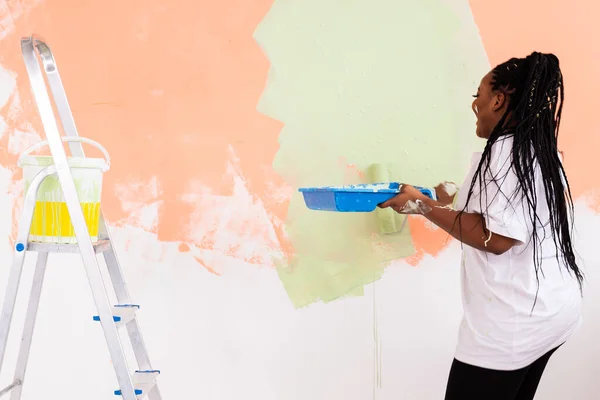 Giovane donna afro-americana felice pittura parete interna con rullo di vernice in nuova casa. Una donna con rullo che applica vernice su un muro. — Foto Stock