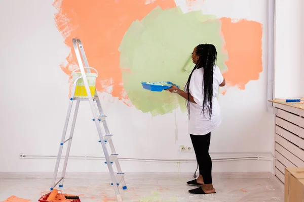 Frumoasă gospodină africană americană pictând perete. Conceptul de renovare, redecorare și reparații . — Fotografie, imagine de stoc