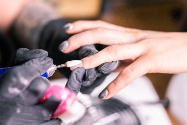 Manikürcü kadının yakın çekimi, manikür makinesi kullanarak müşterilerin tırnaklarındaki jöle parlatmasını kaldırıyor. Manikür ustası güzellik salonunda elektrikli tırnak matkabıyla çalışıyor. Donanım manikür süreci.