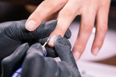 İşlem manikürü yakın çekim. Donanım manikürü için hazırlık. Lastik eldivenli güzellik uzmanı tırnak derisini kesip çivileri işliyor..