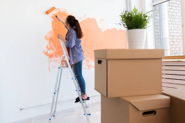 Smiling woman painting interior wall of home. Renovation, repair and redecoration concept.