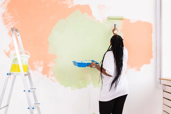 Happy African American woman painting wall in her new apartment. Renovation, redecoration and repair concept.