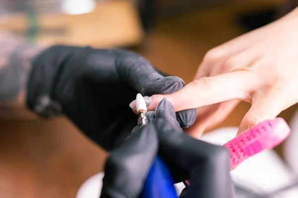 女性のマスターは、サロンでマニキュア中にネイルポリッシュを削除するために電気機械を使用しています。クローズアップハードウェアマニキュア。手のケアの概念。フライス盤による爪の女性マニキュリストのクリーニング — ストック写真
