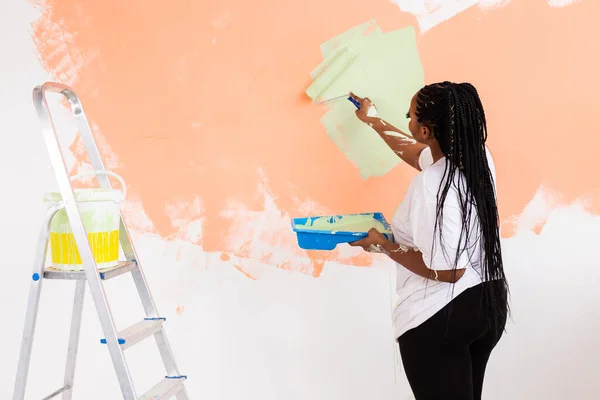 Giovane bella donna afroamericana pittura muro nel suo nuovo appartamento. Concetto di ristrutturazione e ridecorazione. — Foto Stock