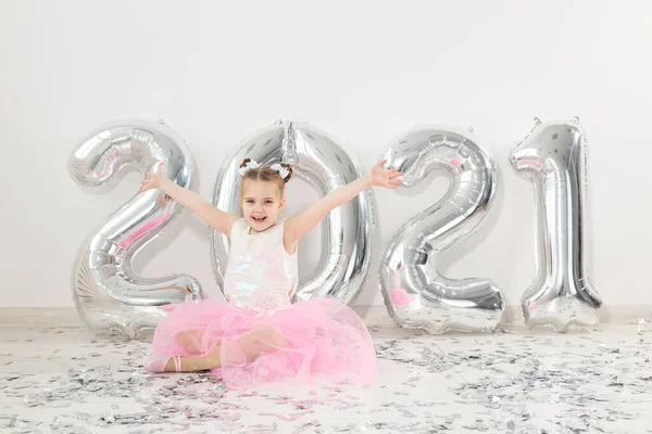 New year, holidays and celebration concept - Little child girl sitting near with numbers balloons 2021