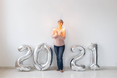 Yeni yıl kutlaması ve parti konsepti - Beyaz arka planda gümüş 2021 balonları yakınında maytaplı mutlu genç kadın.