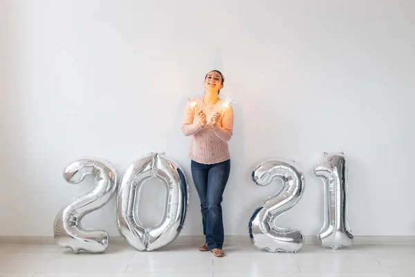Újévi ünneplés és party koncepció - Boldog fiatal nő csillagszórók közelében ezüst 2021 léggömbök fehér alapon. — Stock Fotó