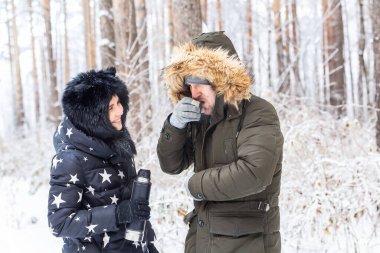 Mevsim ve yürüyüş konsepti - Mutlu çift kış ormanında sıcak çay içiyor