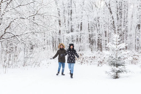 젊고 아름다운 한 쌍이 눈덮인 공원에서 달리고 손을 잡고 즐거운 시간을 보내고 있다. 발렌틴 데이 컨셉이야. 겨울 계절. — 스톡 사진