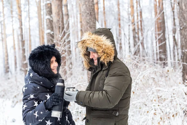 O par jovem no amor bebe uma bebida quente de uma garrafa térmica e gosta da natureza de inverno. — Fotografia de Stock