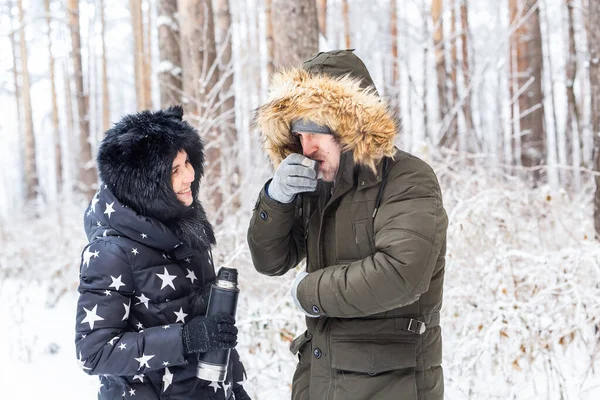 Sezon i koncepcja spaceru - Szczęśliwa para pije gorącą herbatę w zimowym lesie — Zdjęcie stockowe