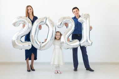 Genç, mutlu aile babası ve kızı beyaz arka planda 2021 numaralı balonların yanında duruyorlar. Yeni yıl, Noel, tatil