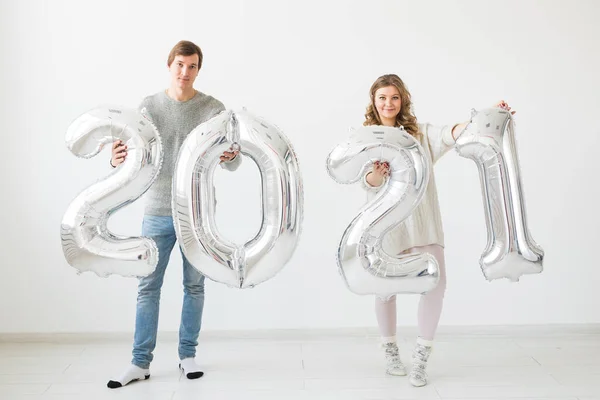 Vacaciones, fiesta y concepto de fiesta - Feliz pareja amorosa sostiene globos de plata 2021 sobre fondo blanco. Celebración de Año Nuevo. — Foto de Stock