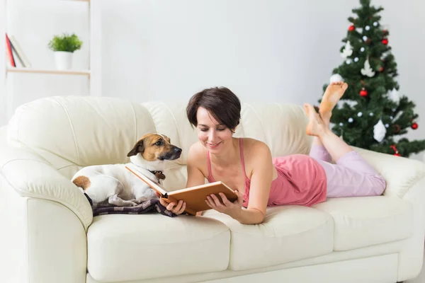 Χριστούγεννα, διακοπές και άνθρωποι έννοια - ευτυχισμένη νεαρή γυναίκα ανάγνωση βιβλίο στο σπίτι. — Φωτογραφία Αρχείου