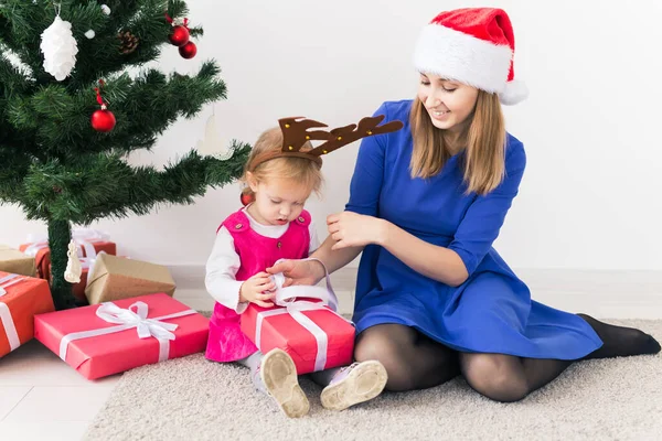 笑顔の母はバックグラウンドで赤ちゃんの娘とクリスマスプレゼントを開きます。冬の季節。母親。メリークリスマス。新年. — ストック写真