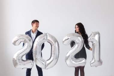 Yeni yıl, kutlama ve tatil konsepti - beyaz arka planda yeni yıl için gümüş balonlardan yapılmış 2021 tabelasıyla eğlenen aşk çifti