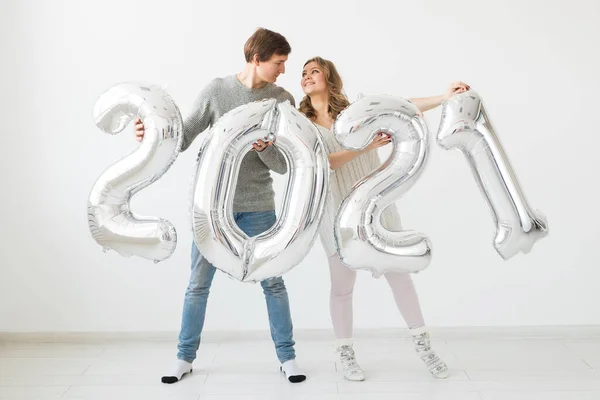 Vacaciones, fiesta y concepto de fiesta - Feliz pareja amorosa sostiene globos de plata 2021 sobre fondo blanco. Celebración de Año Nuevo. — Foto de Stock