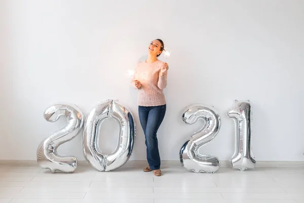 Celebración de Año Nuevo y concepto de fiesta - Mujer joven feliz con brillantes cerca de plata 2021 globos sobre fondo blanco. — Foto de Stock