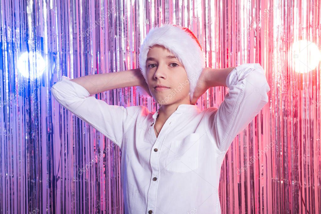 Christmas time. Teen boy with Santa Claus Hat over shiny festive background. Christmas holidays concept.