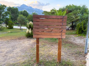 Palmiye ağaçları ve dağ manzaralı bir parkta ahşap tabela var. Navigasyon, turizm ve açık hava oryantasyonu manzara, seyahat ve doğal çevre rehberliğini yansıtır..