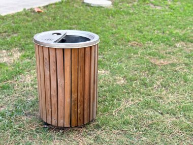 Metal kapaklı ahşap çöp tenekesi parktaki çimlerin üzerinde duruyor. Ekoloji, sürdürülebilirlik ve atık yönetimi temizlik, kentsel hizmet ve açık hava hizmetlerini yansıtıyor.