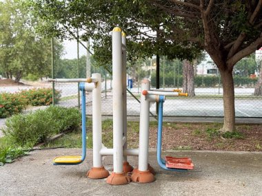 Parkın yanındaki tenis kortunun yanında pedalları ve barları olan açık hava eğitim makinesi. Spor, hareket ve sağlık günlük yaşam tarzında toplumsal etkinlik, güç ve sağlık gösteriyor.