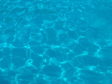 Yüzme havuzunda güneş ışığı yansıması olan mavi su yüzeyi. Boş zaman, dinlenme ve yaz yaşam tarzı berraklık, ferahlık ve su rahatlığı ile temsil edilir.