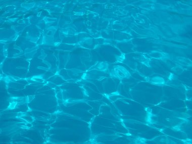 Yüzme havuzunda güneş ışığı yansıması olan mavi su yüzeyi. Boş zaman, dinlenme ve yaz yaşam tarzı berraklık, ferahlık ve su rahatlığı ile temsil edilir.