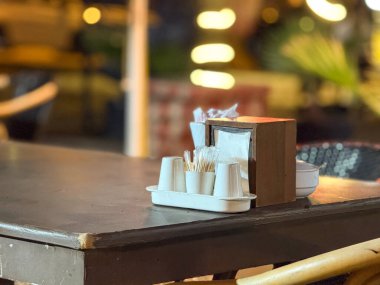 Bir kafede servis için düzenlenmiş peçete tutacağı, kürdanı ve fincanı olan masa. Misafirperverlik, hijyen, tek kullanımlık eşyalar, akşam yemeği ve restoran ayrıntıları.