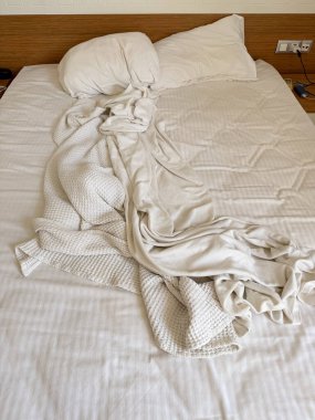 Otel odasının içinde yastıklı ve battaniyeli yapılmamış bir yatak. Konukseverlik, seyahat, konaklama, dinlenme, yaşam tarzı ve günlük yaşam ortamı