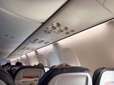 Uçağın tavanındaki havalandırma, ışık ve yolcuların biniş sırasında aşağıda oturduğu manzara. Seyahat, havacılık ve kabinin içinde uçuş hazırlığı deneyimi.