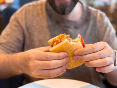 Isırılmış sandviçi gözle görülür dolguyla tutan ellerin yakın çekimi. Günlük yeme alışkanlıklarında yiyecek, tüketim ve yaşam tarzı anları.