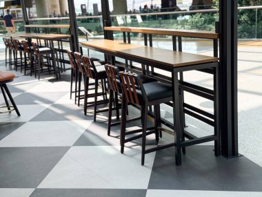 Halka açık bir salonda geniş pencerelerle düzenlenmiş yüksek tabureli uzun ahşap masalar. Modern konukseverlik alanlarında seyahat yaşam tarzı, yemek ve sosyal atmosferin temsili