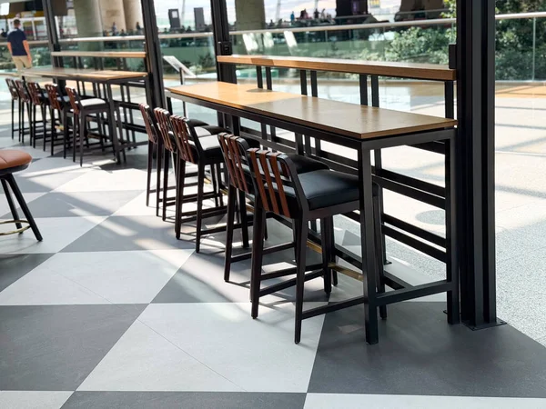 Halka açık bir salonda geniş pencerelerle düzenlenmiş yüksek tabureli uzun ahşap masalar. Modern konukseverlik alanlarında seyahat yaşam tarzı, yemek ve sosyal atmosferin temsili