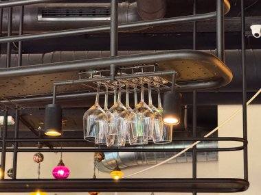 Modern barın içindeki tavan rafında baş aşağı asılı şarap kadehleri. Konukseverlik, yemek servisi ve yaşam tarzı atmosferi içki takımı, organizasyon ve modern mobilyaların birleşimi