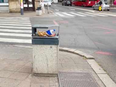 Şehir caddesinde yaya geçidi yakınında plastik şişe ve kağıt atığı olan umumi çöp kutusu. Modern şehir yaşamında çevre kaygısı, atık imhası ve sağlık sorunları