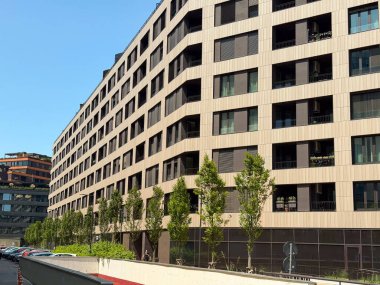Mavi gökyüzünün altında balkonları ve pencereleri olan modern apartman binasının ön cephesine yakın plan. Konut yatırımını sembolize eden çağdaş mimari, konut geliştirme ve kentsel yaşam tarzı