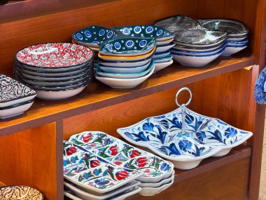 Ahşap raflarda seramik tabaklar ve çiçek desenleri var. Kültürel işçilik, dekoratif hizmetler ve günlük yaşamın zanaatkar mirası.